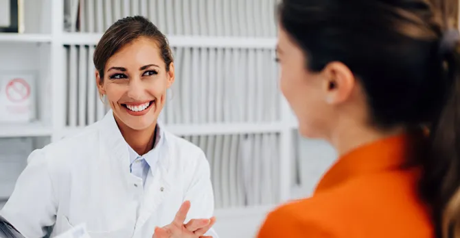 A hospital caregiver assists a patient who is standing at her station.