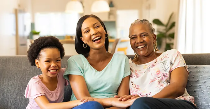 Three generations of females sit together on a sofa and share a laugh: mother, daughter, and grandmother.