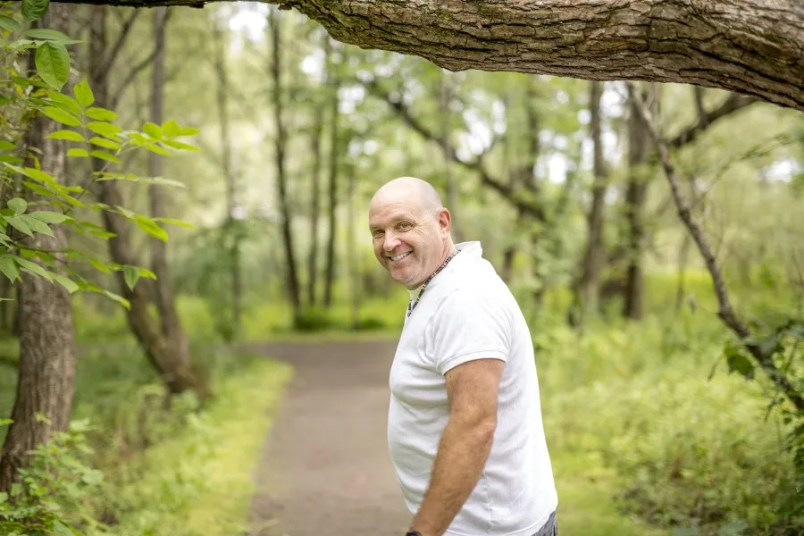 man in white t-shirt with thyroid issue walking on trail in woods