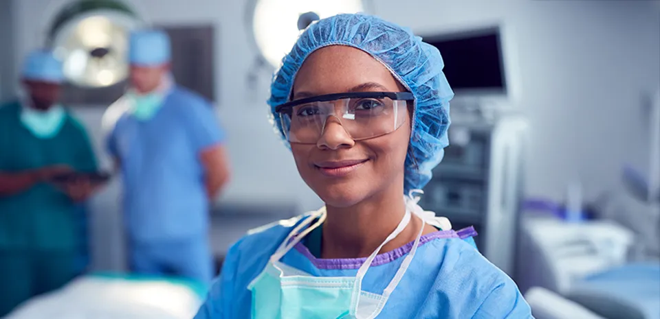 A CRNA in an operating room, smiling and looking at the camera.