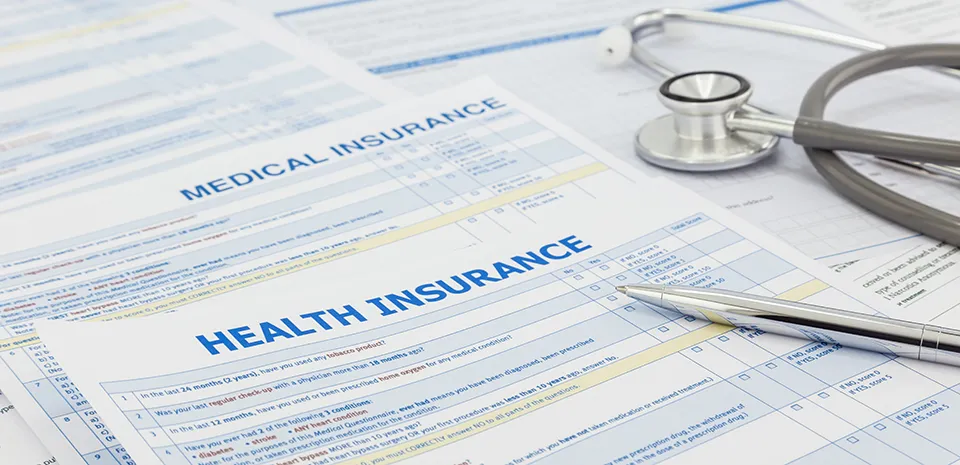 A pen and a stethoscope lay on top of a number of insurance forms.
