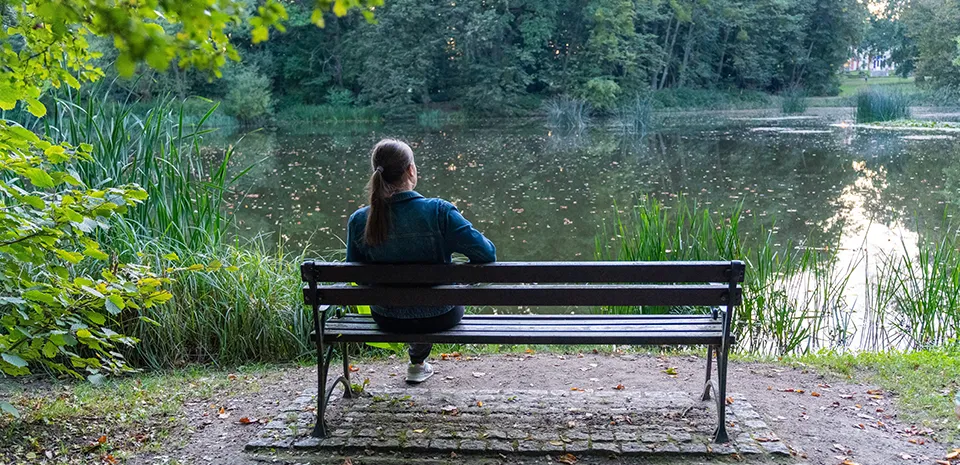 young woman sitting on bench near a pond