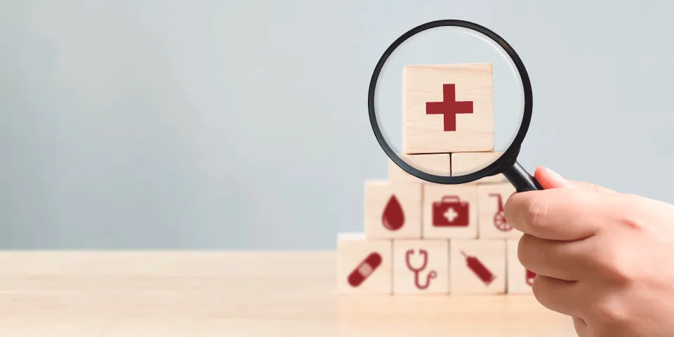 Medical icon blocks stacked in a pyramid, with a red cross at the top highlighted by a magnifying glass.