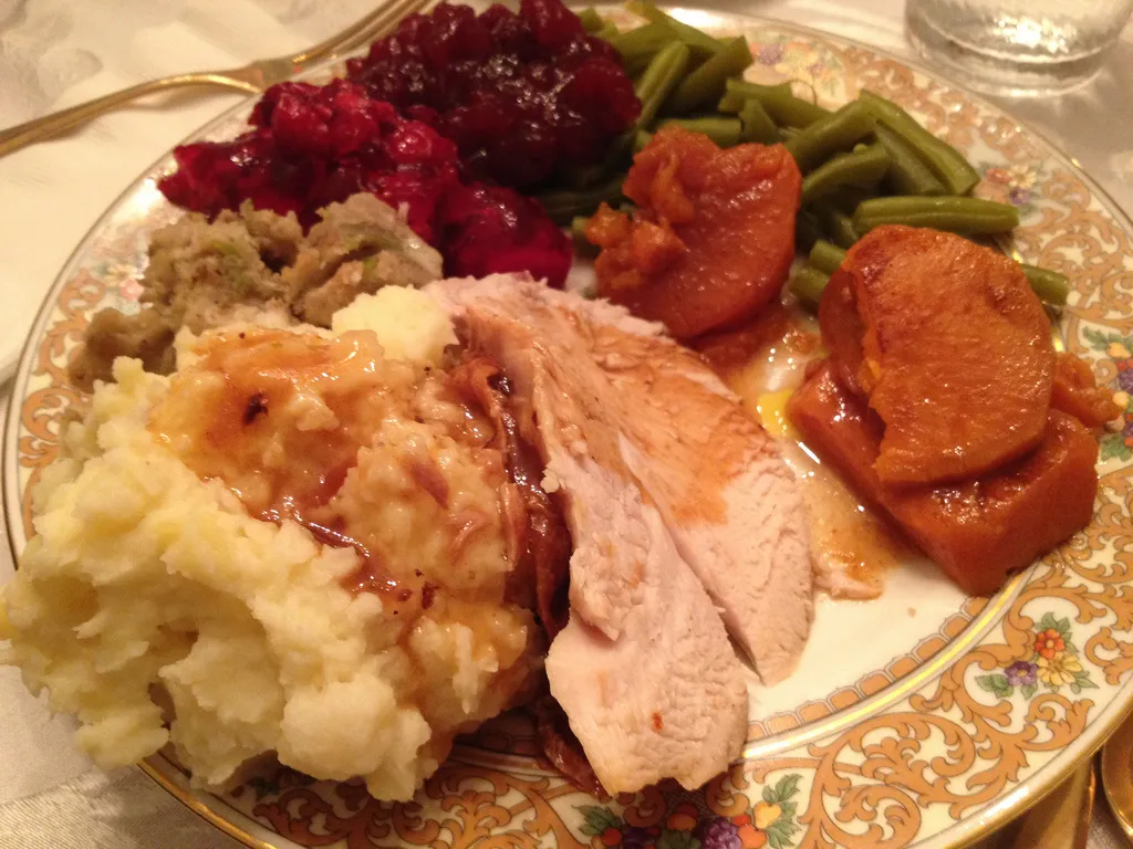 A closeup of a Thanksgiving dinner with turkey, masked potatoes, stuffing, and vegetables.