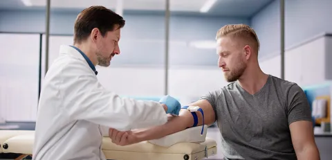 A health care worker takes blood from a patient in the phlebotomy lab.