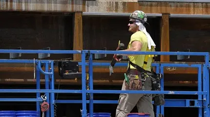A worker uses a towel for protection from the sun while working in temperatures above 90 degrees at a building construction site, Thursday, June 20, 2024, in Boston.