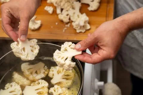 man's hands placing chopped cauliflower into a pot on the stove