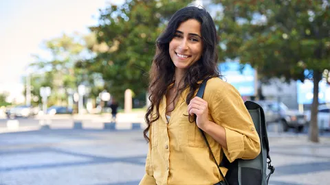 Student intern with long, dark, wavy hair wearing a mustard yellow button-up dress shirt with a backback over her shoulder