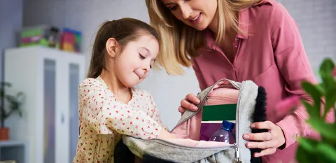 mom helping daughter pack backpack for school