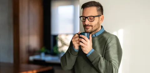 Man with eyes closed holding a warm cup of coffee in a kitchen practicing mindfulness