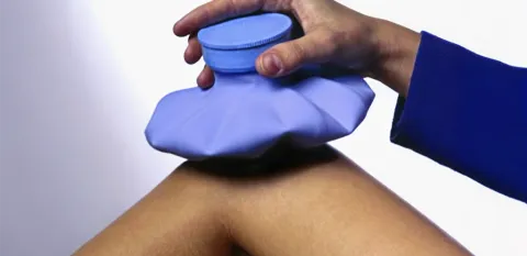 Someone's hand is holding a blue ice bag in place on their bent knee.