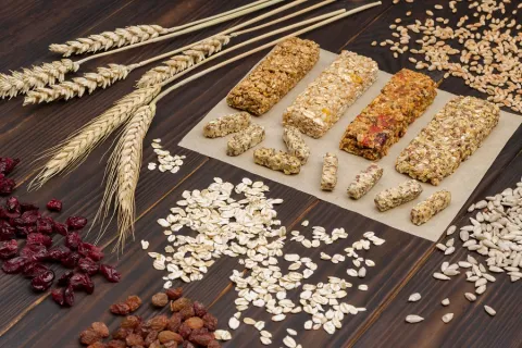 Multiple granola bars are on a table with various grains, oats, and wheat.