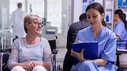 A young woman takes notes while speaking to a a patient in a wheelchair.