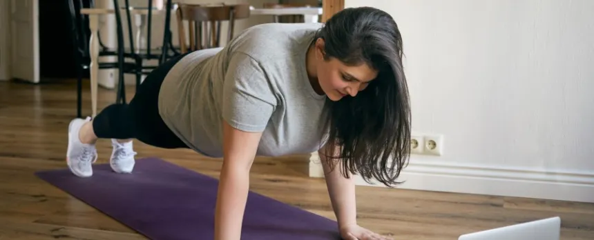 Woman concerned about spine health doing a plank in front of laptop
