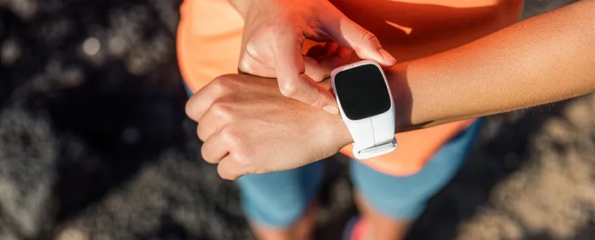 A woman looks at the fitness tracker on her wrist while walking outside.