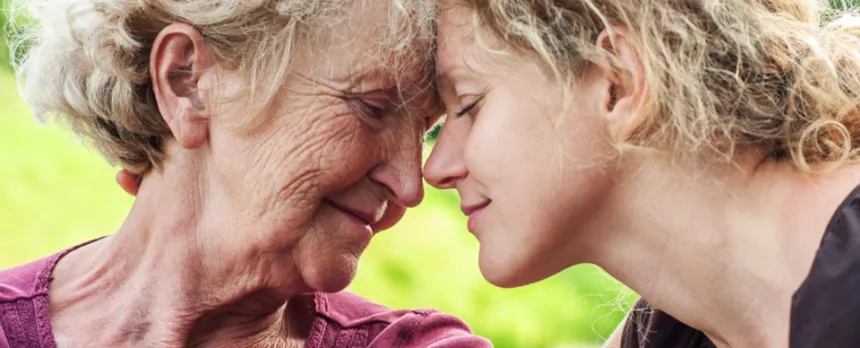 A grandmother and her granddaughter lean into each other, foreheads touching.