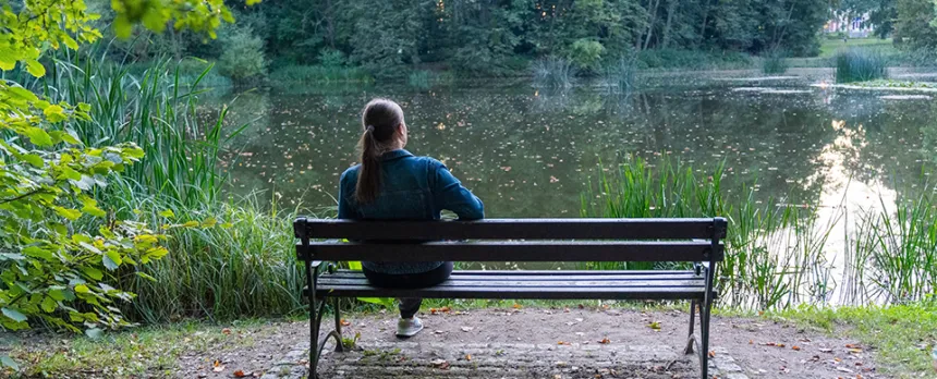 young woman sitting on bench near a pond