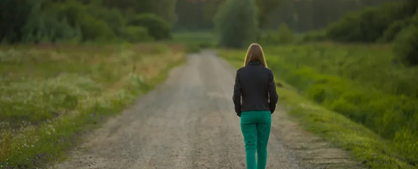 woman walking down a dirt road towards the sunset