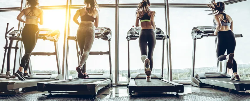 Multiple women are shown on treadmills from behind.